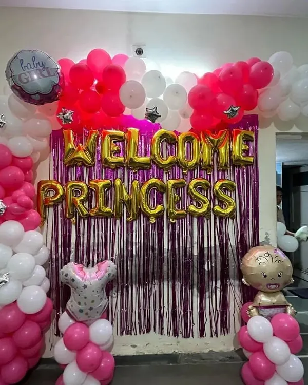 A complete "Welcome Princess" decoration for a baby girl's homecoming. This setup features a vibrant pink and white balloon arch, gold foil letters, and a shimmering purple tinsel curtain for a festive photo backdrop.