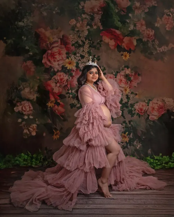 A portrait of pure royalty. The mother-to-be, wearing a delicate crown and the stunning pink ruffled gown, looks every bit the queen she is against a beautiful floral backdrop.