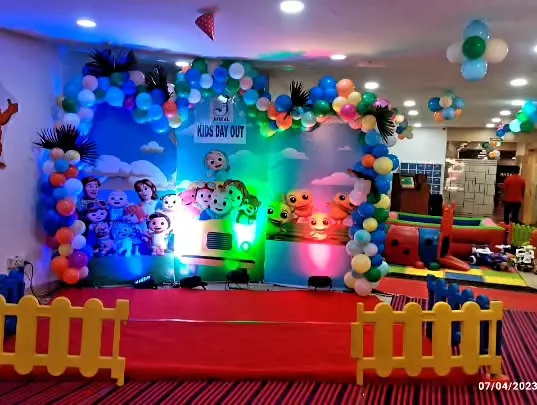 A vibrant Cocomelon stage setup for a "Kid's Day Out" event. This decoration features a large, colorful printed backdrop with all the favorite characters, framed by a playful balloon arch.