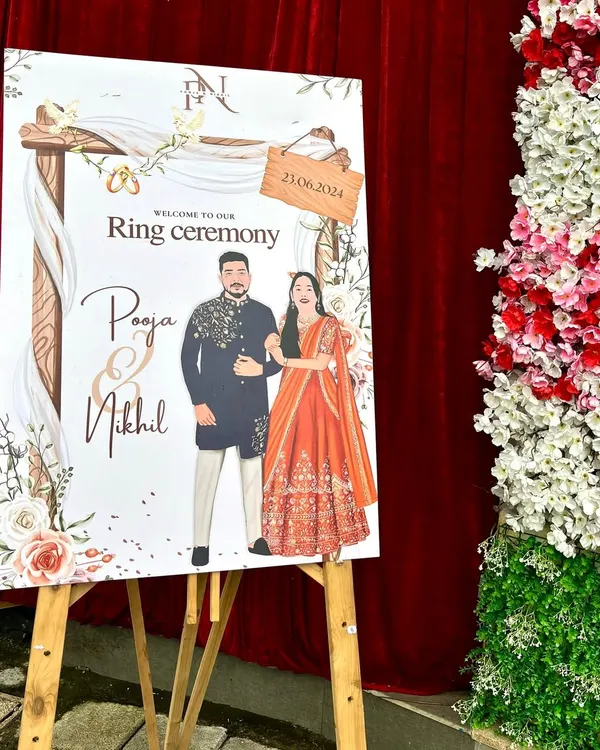 The final printed welcome board for Pooja and Nikhil's ring ceremony, set up on an easel at the event venue. It looks stunning next to the floral decorations.