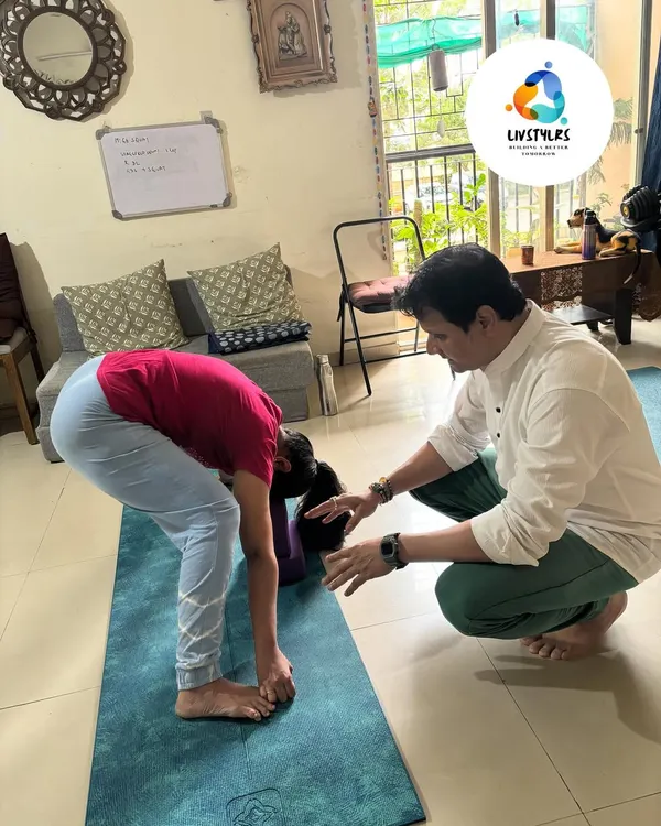 I am providing a gentle adjustment to a client in a forward fold (Uttanasana). This hands-on assist helps her deepen the stretch safely and release tension in her hamstrings and lower back.
