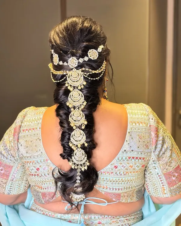 A stunning messy braid adorned with a beautiful, cascading hair ornament. This is a perfect hairstyle for a sangeet or reception, combining traditional and modern elements.