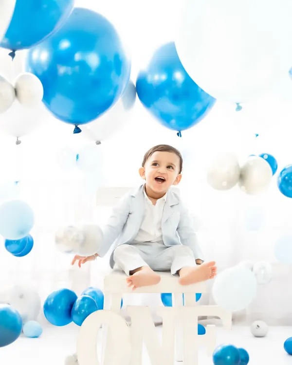 A baby boy celebrates his first birthday in a classic blue and white balloon-filled setup. His joyful expression and the festive atmosphere perfectly capture the happiness of this major milestone.