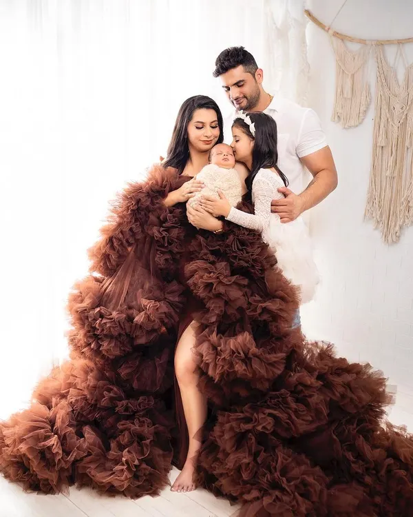 A stunning family portrait featuring the mother in a dramatic ruffled gown, holding her newborn while the father and older sister look on. This is a perfect example of a full family newborn photoshoot.