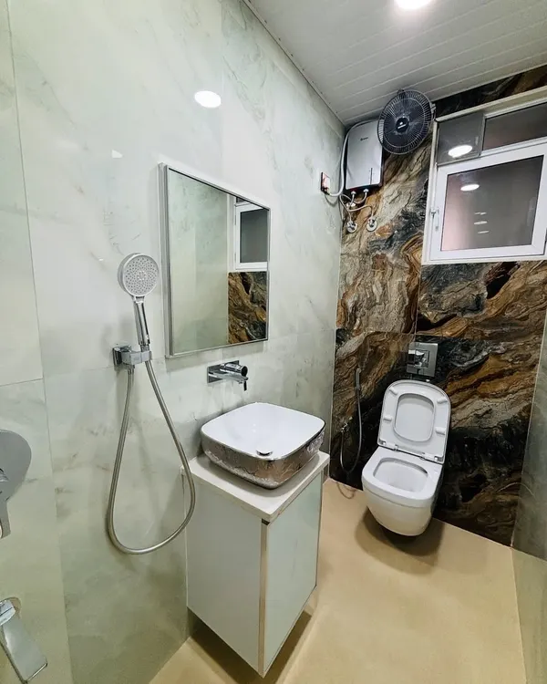 A full view of a remodeled bathroom. The design features a combination of light marble-finish wall tiles and a dramatic, dark-veined accent wall behind the wall-mounted toilet.