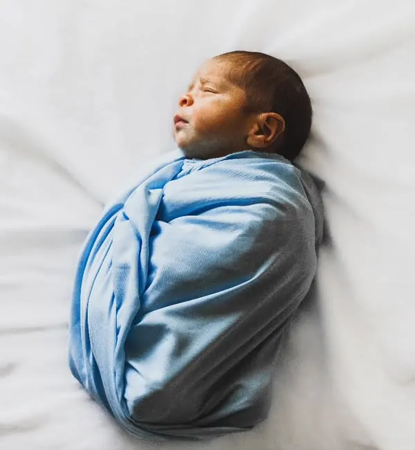 A beautifully simple newborn portrait. This baby boy is swaddled snugly in blue on a clean white background, emphasizing his peaceful, sleeping form.