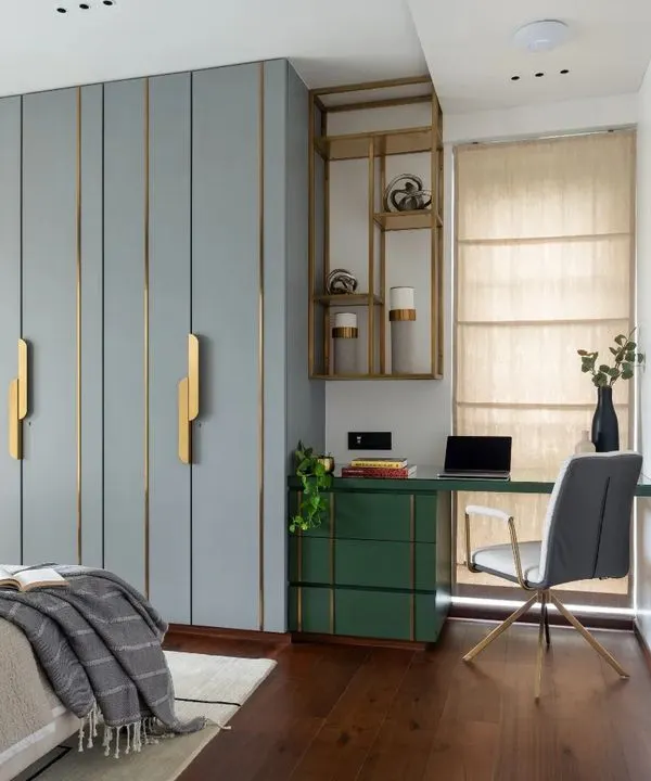 This master bedroom at Park West features a custom wardrobe with a serene blue-grey finish and elegant brass inlay details. Adjacent to it, a compact study nook with a vibrant green desk provides a functional workspace without compromising the room's restful feel.
