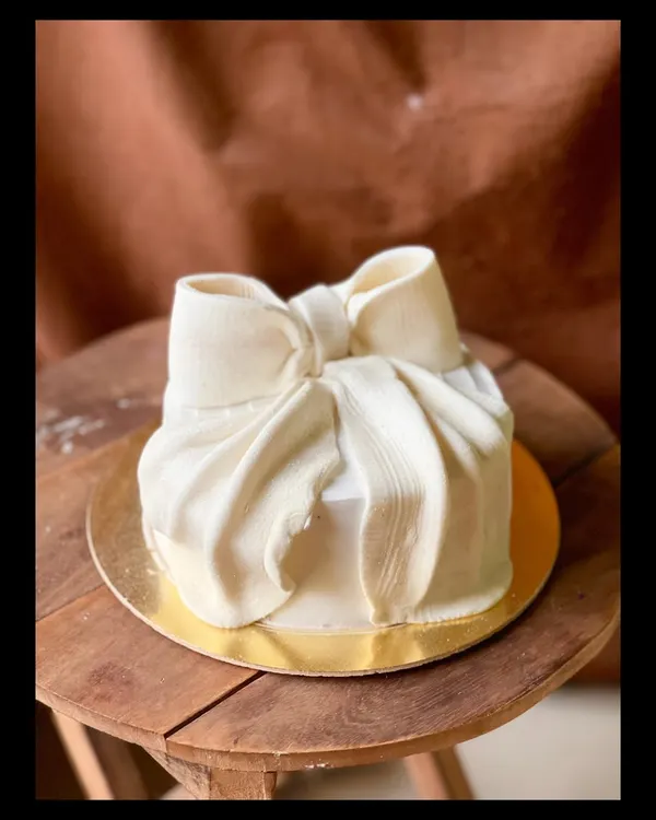 A cake designed to look like a perfectly wrapped gift. This stunning piece features a large, sculpted white chocolate bow on a smooth, square cake.