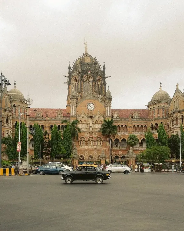 A classic Kaali-Peeli taxi drives past the magnificent Chhatrapati Shivaji Maharaj Terminus. This single frame perfectly unites two of Mumbai's most iconic symbols of transport and architecture.
