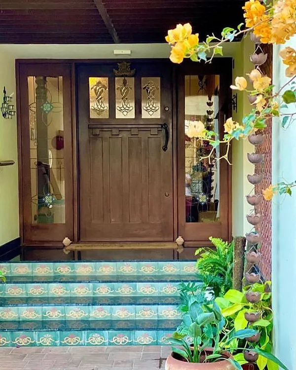 The entrance to Roopa Hariprasad’s Residence features a custom-designed wooden door with intricate glasswork. The steps are adorned with traditional patterned tiles, creating a welcoming and highly personal entryway.