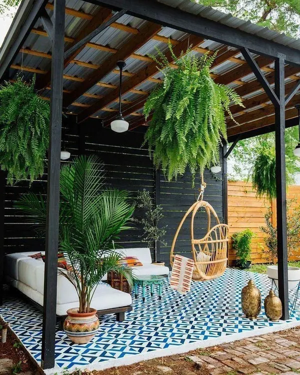 An inspirational design for a covered terrace or patio. This concept uses patterned floor tiles, a dark pergola structure, and lush hanging plants to create a stylish and shaded outdoor lounge.