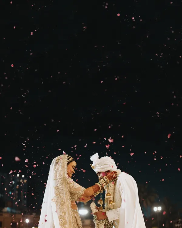 A stunning, artistic shot of the couple during their varmala ceremony, with a shower of petals against the night sky. This is a moment of pure magic.