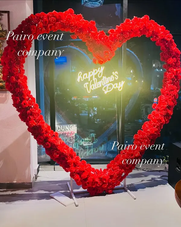 A stunning, large heart frame made entirely of artificial red roses, with a "Happy Valentine's Day" neon sign. This makes a perfect photo opportunity for any event.