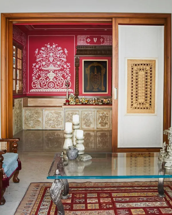 A view into the hand-painted temple in Hyderabad, seen from the living area. The striking red walls, covered in traditional motifs by Jaipur artists, create a sacred space that feels both powerful and deeply personal. It took two artists nearly three months to bring this vision to life.