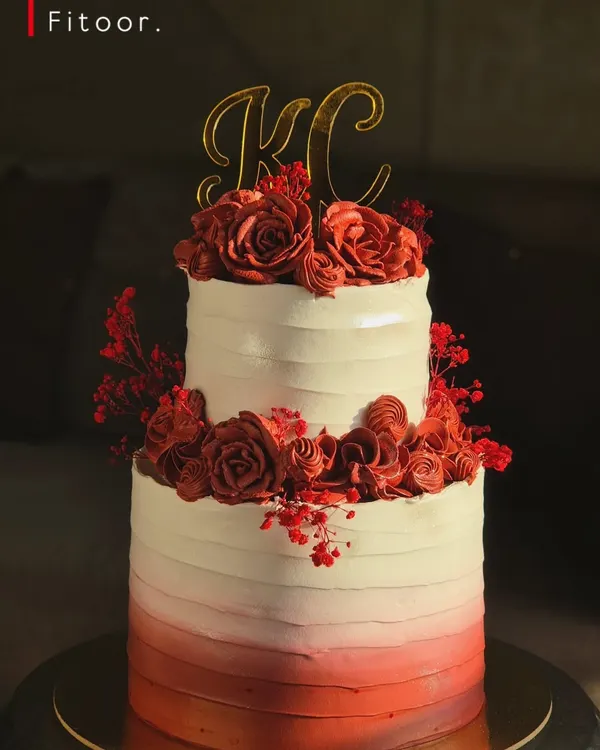 A stunning two-tier engagement cake with a red ombre buttercream finish and handcrafted red roses. The custom 'KC' topper makes it a truly personal centerpiece for a special celebration.