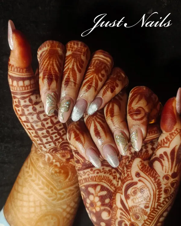 A stunning example of bridal nails designed to complement intricate henna. This set features long, almond-shaped extensions with a mix of silver glitter and delicate, hand-painted leaf patterns.