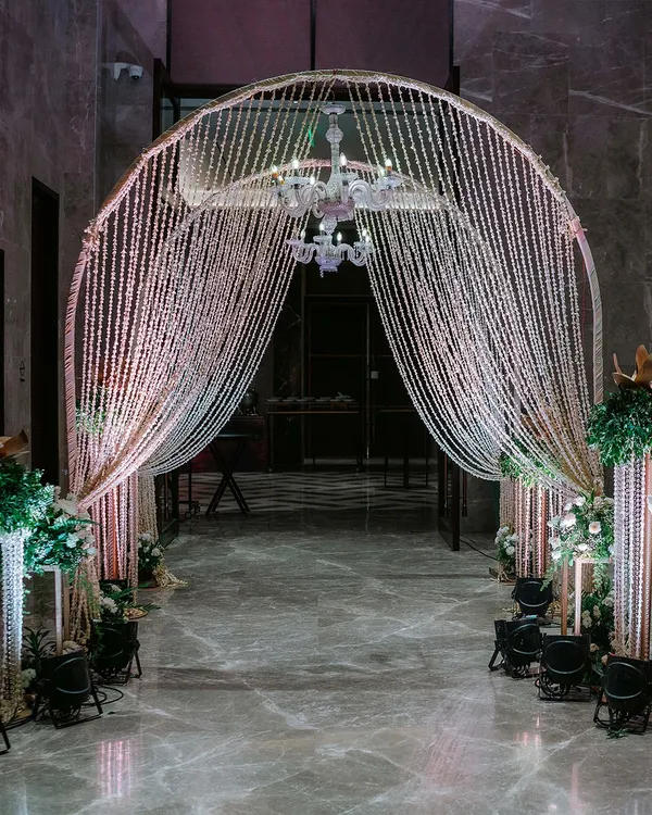 We created this spectacular entrance arch using curtains of shimmering beads and a crystal chandelier. Flanked by pillars of white flowers, it provides a glamorous and magical welcome for an evening reception.