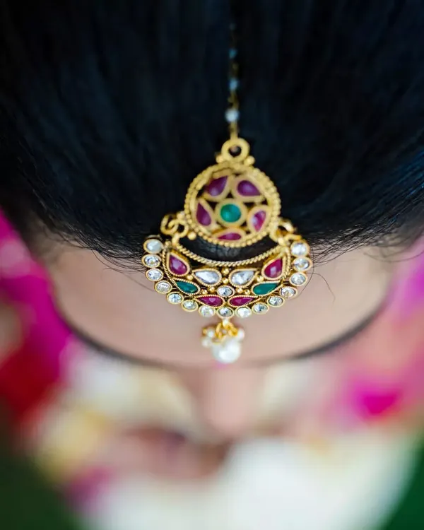A top-down macro shot of a bride's 'maang tikka', highlighting the beautiful kundan and gemstone work in her wedding jewelry.