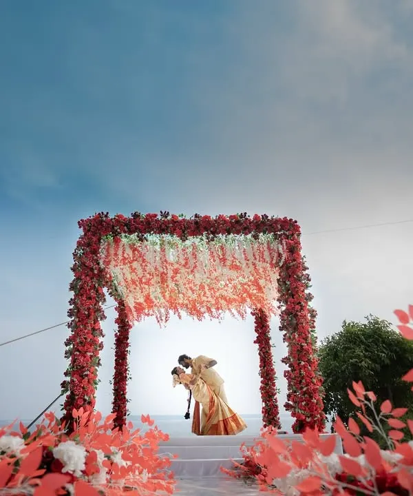 A truly epic destination wedding shot. The couple shares a kiss under a magnificent floral mandap, set against the sky and sea. This is what destination wedding dreams are made of.