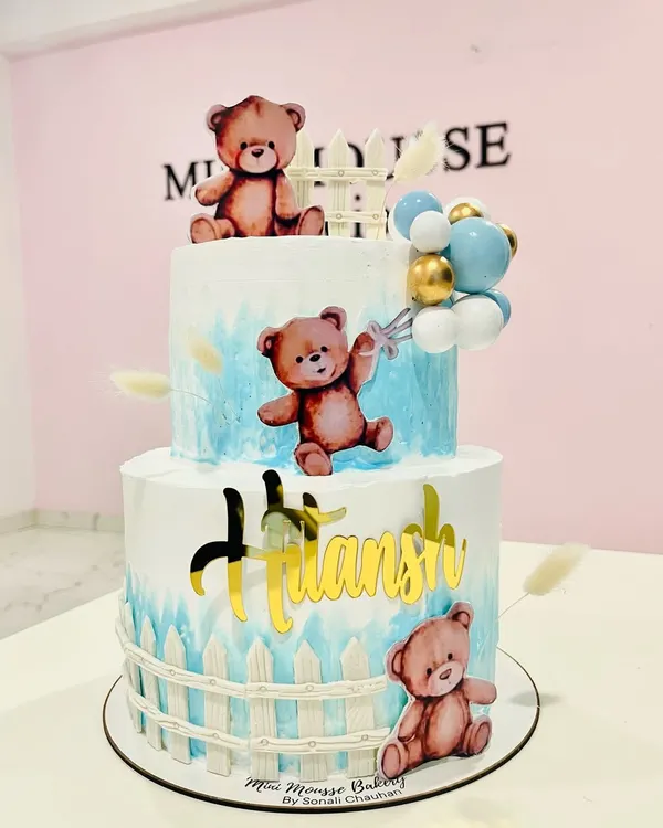 A beary cute two-tier cake for a little boy's celebration. This teddy bear themed cake features a soft blue watercolor effect, a picket fence design, and adorable bear toppers.