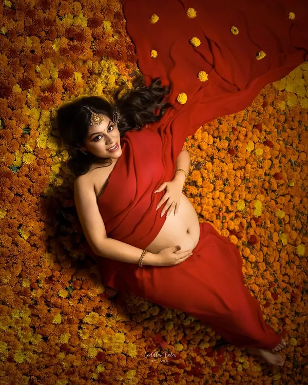 In full bloom. This stunning overhead shot shows the mother-to-be lying on a bed of vibrant marigolds, her red saree spreading out like a flower. It's a modern, artistic take on a traditional theme.