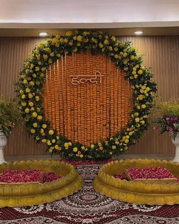 This is a classic Haldi setup for an indoor event. We used a large circular backdrop made entirely of marigold strings and a floral border, with two traditional brass urlis for the ceremony.