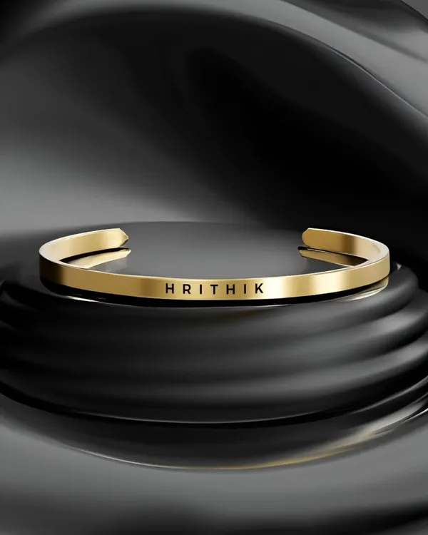 A stunning product shot of the gold-plated cuff bracelet, professionally engraved with the name 'HRITHIK'. The clean font and polished finish create a bold, elegant look.