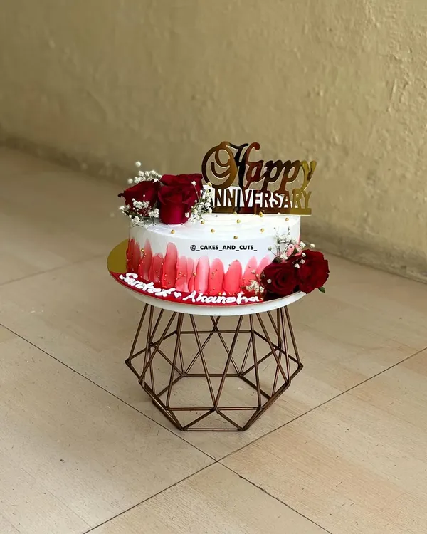 A beautiful anniversary cake with a red ombre design, fresh red roses, and a golden "Happy Anniversary" topper.