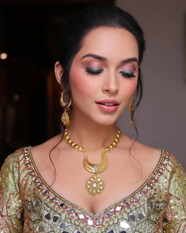 A close-up of the carnival-inspired Mehendi makeup. The eyes are the focus, with a blend of pink and green eyeshadow, a sharp wing, and delicate gold dust and studs for a truly unique look.