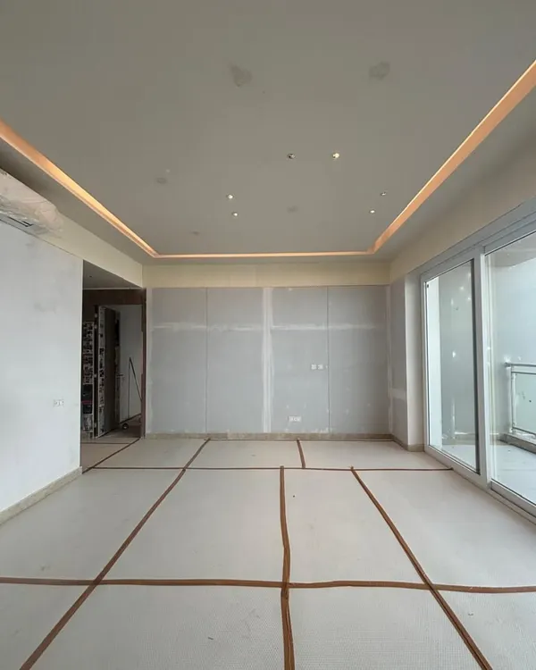 A blank canvas full of potential. This is a work-in-progress shot of a living room, with floor-to-ceiling windows promising abundant light. The markings on the floor map out the future placement of furniture, the first step in transforming this empty shell into a home.