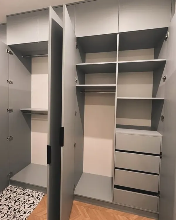 This open hinged wardrobe shows a practical layout with double hanging rods, multiple shelves, and a bank of four deep drawers. The cool grey finish and handleless design give it a clean, modern aesthetic.