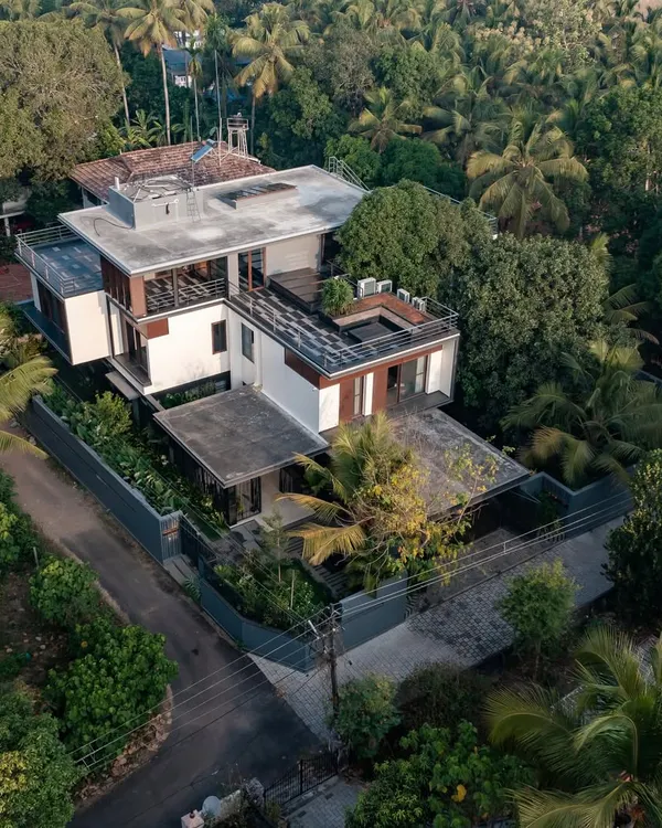 An aerial view and a dusk shot of the Mango Tree Yard residence in Thrissur, showing the pavilion-style layout nestled within a lush, tropical landscape.