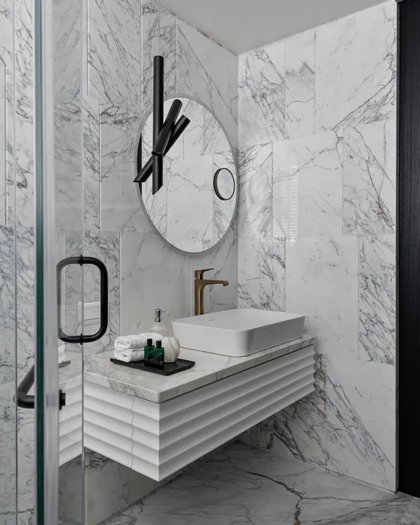 This bathroom makeover is all about bliss where design and comfort unite. The space is clad in dramatic veined marble, with a custom fluted vanity and a sculptural mirror, transforming it into a sleek and modern sanctuary.