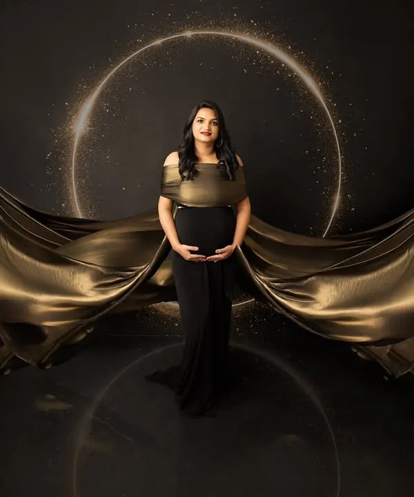 A breathtaking fine art portrait featuring a mother-to-be in a stunning black and gold gown. The fabric flows dramatically, creating a powerful and elegant silhouette that celebrates the beauty of pregnancy.
