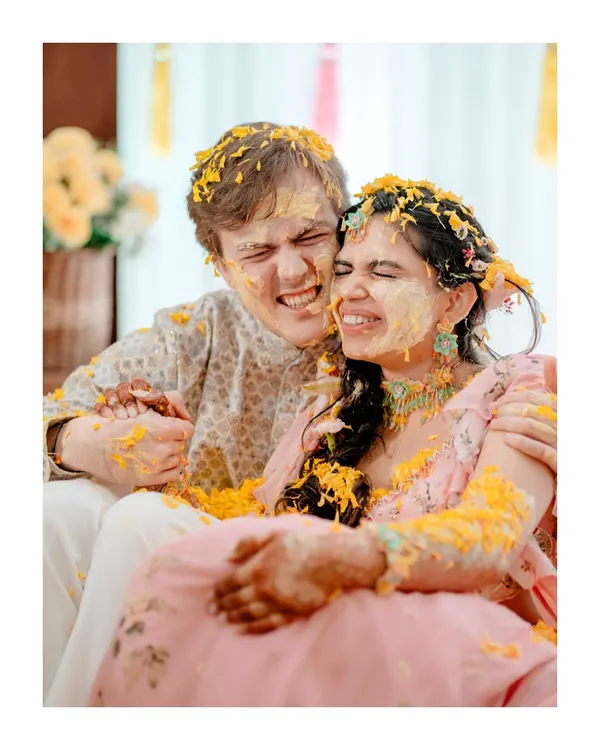 A moment of pure, messy fun. This candid shot of the couple covered in haldi and flower petals perfectly captures the playful spirit of the ceremony.