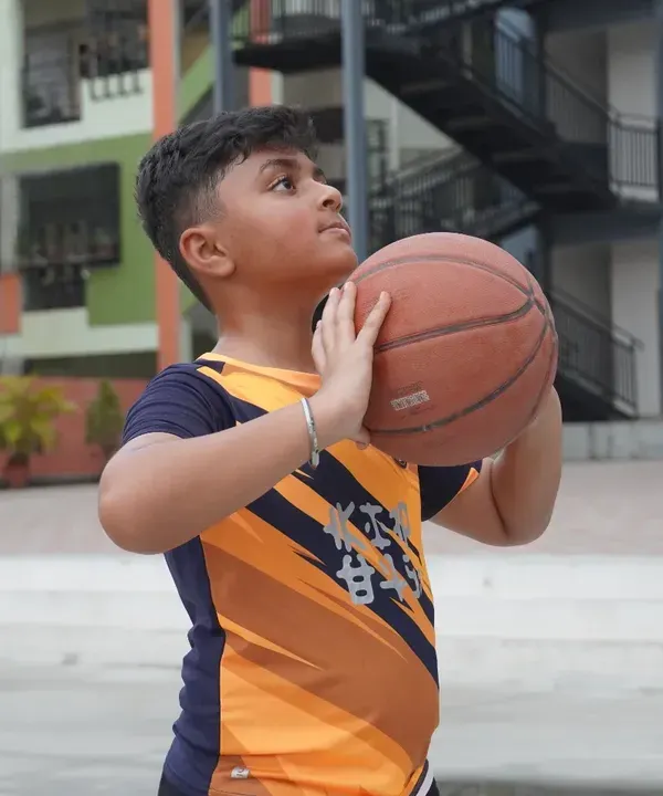 A young player focuses on his shooting form, holding the basketball correctly before taking a shot. We teach the fundamentals of a perfect jump shot, building muscle memory and confidence from the very first day.