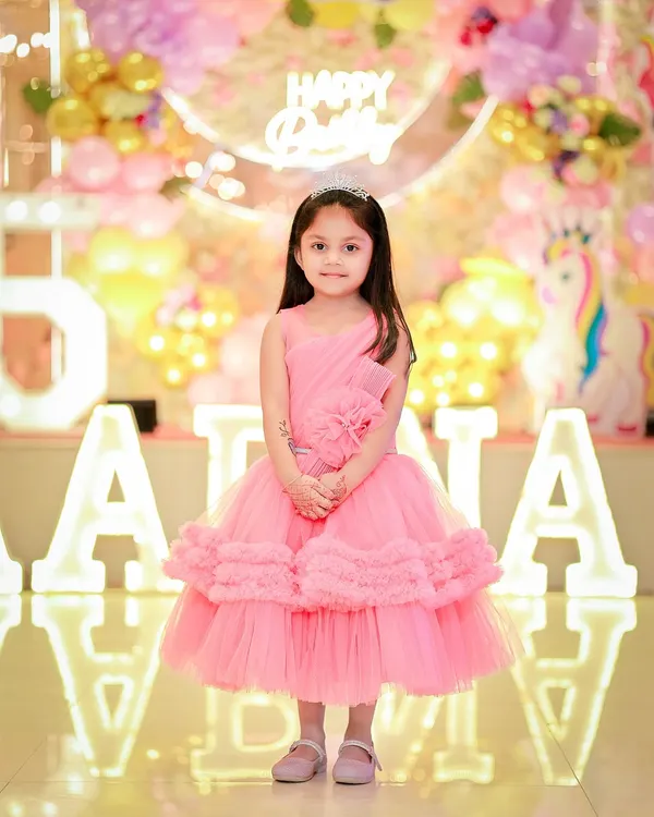 A sweet portrait of the birthday girl in her pink party dress, standing in front of her name in lights.
