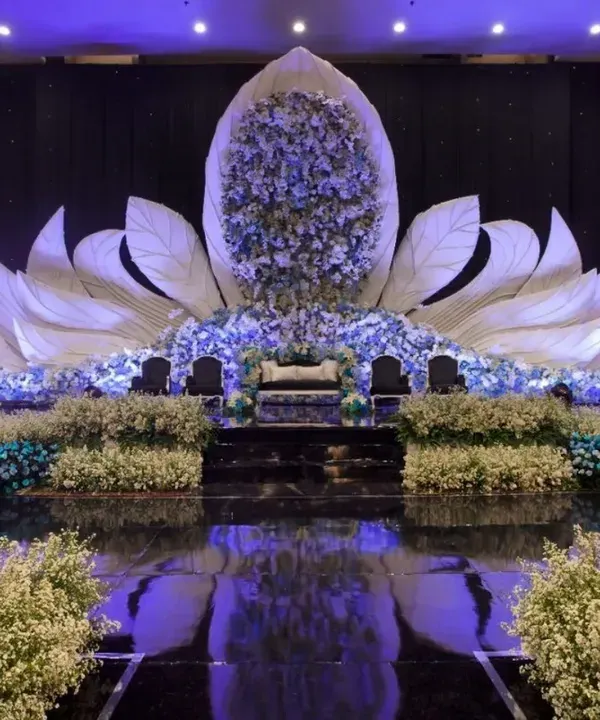 This is the kind of showstopper stage I love to create. The design features a massive blooming lotus structure, filled with flowers and lit from within to create a magical glow. The reflective flooring mirrors the entire setup, making the venue feel grand and immersive for your reception.