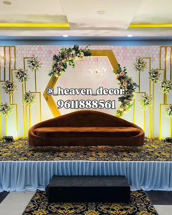 We designed this modern reception stage with a striking hexagonal floral arch and geometric gold frames. The elegant lighting and plush velvet sofa create a sophisticated centerpiece, perfect for a contemporary wedding or engagement celebration.