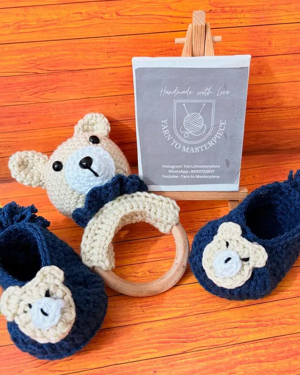 This adorable baby boy set includes a pair of navy blue booties with bear faces and a matching bear rattle. It's made from soft, safe yarn, perfect for a newborn gift.
