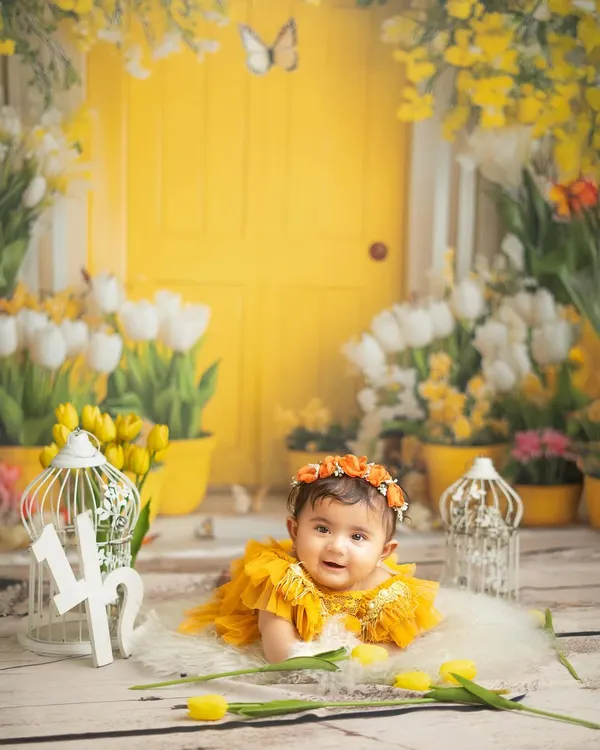 Halfway to one. This cheerful sitter session with a bright yellow door and tulips is perfect for celebrating the six month milestone. Her happy expression says it all.