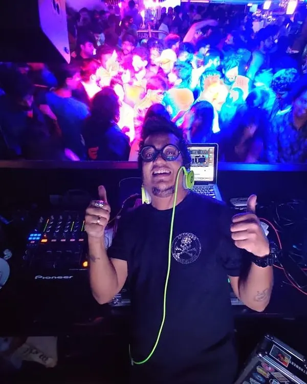 This is my view from the DJ booth, my favorite place to be. I am giving a thumbs up to the camera, with a packed, high-energy dance floor visible on the screen behind me, showing exactly the kind of party atmosphere I create.