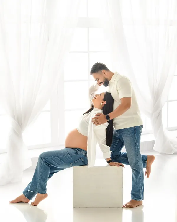A playful and intimate moment between the expecting couple. Dressed in casual jeans and white shirts, they share a laugh in our bright, sunlit studio, creating a relaxed and authentic portrait.