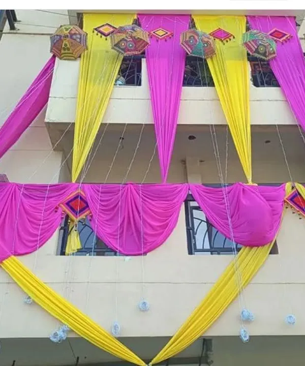 An example of our house exterior decoration for a wedding. We use bright pink and yellow drapes, along with decorative umbrellas and hangings, to adorn the building's facade.