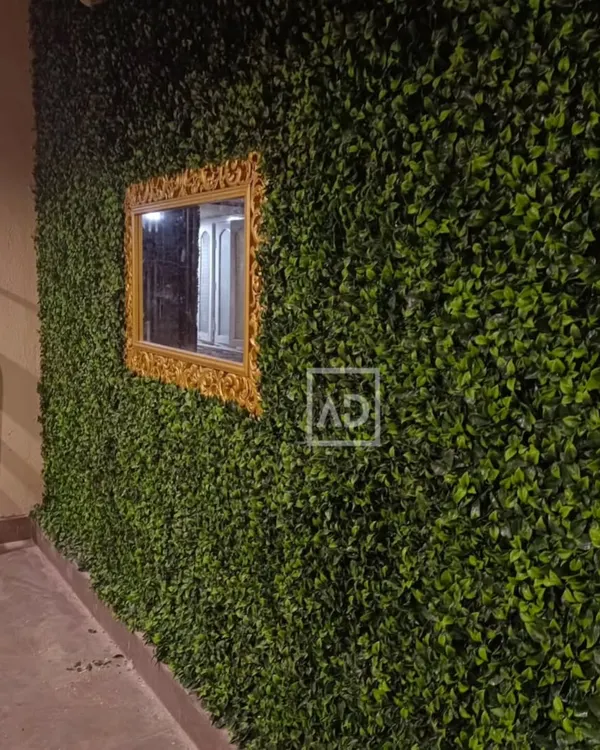 An artificial vertical garden installed on an exterior wall, with a cutout for an ornate gold-framed mirror. This creates a beautiful and surprising feature, blending classic and natural elements.