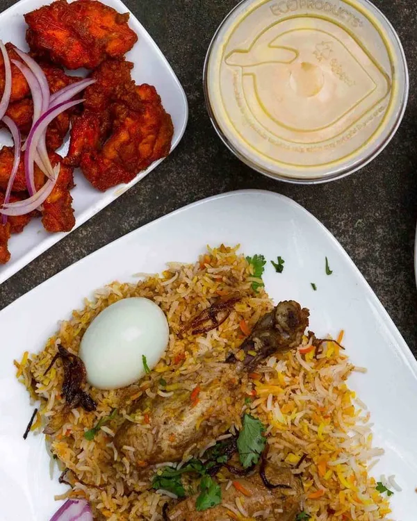 A complete Mughlai meal featuring my signature Chicken Biryani with a boiled egg, a side of rich chicken curry, spicy chicken 65 starters, and a cooling dip. This is the kind of quality and variety you can expect when you order from me.