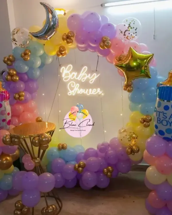 A gorgeous pastel-themed baby shower decoration with a full balloon ring. This setup includes a 'Baby Shower' neon sign and foil balloons shaped like baby bottles.
