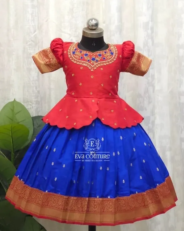 A vibrant pattu pavadai with a modern peplum top. The red blouse has intricate maggam work, and it pairs beautifully with the royal blue skirt that has a traditional gold zari border.