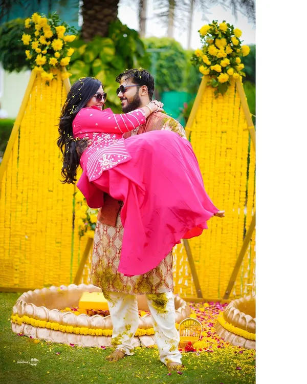 A classic Bollywood-style lift! This fun and romantic shot from a Haldi ceremony, set against a vibrant marigold backdrop, captures the playful love between the couple.