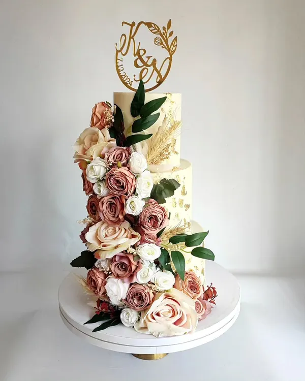 A breathtaking three-tier wedding cake featuring a cascade of dusty rose and cream flowers. This design is the epitome of romance and elegance, perfect for a grand celebration.